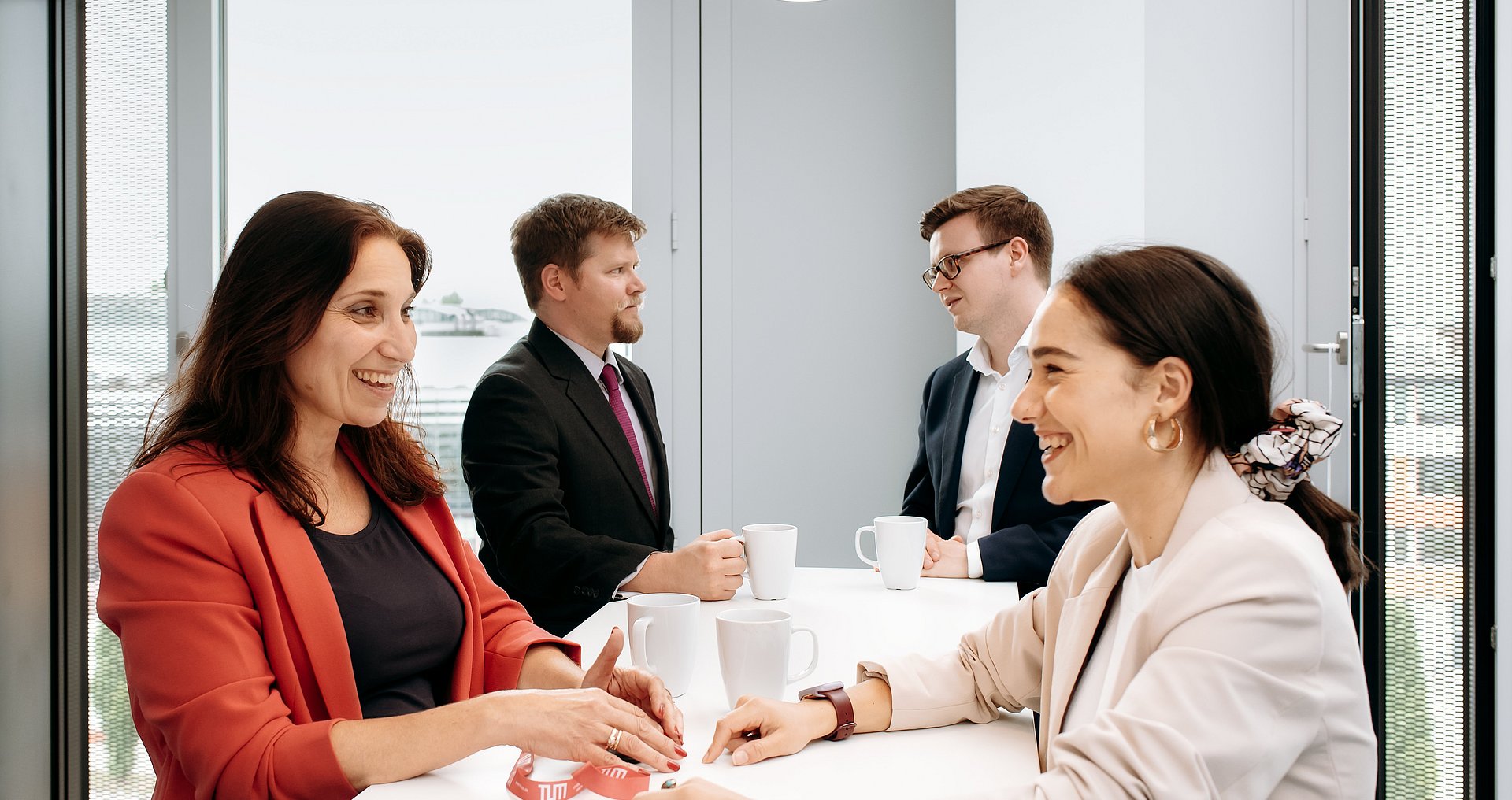 A get-together at the workplace Two women and two men come together at a bar table and chat while drinking a cup of coffee.